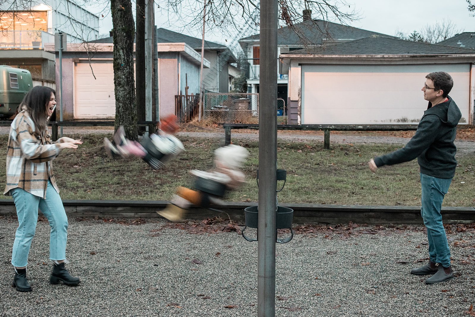 Mum and Dad pushing the kids on the swings while having family photographs taken by Sea to Sky Studios at a park in East Vancouver .